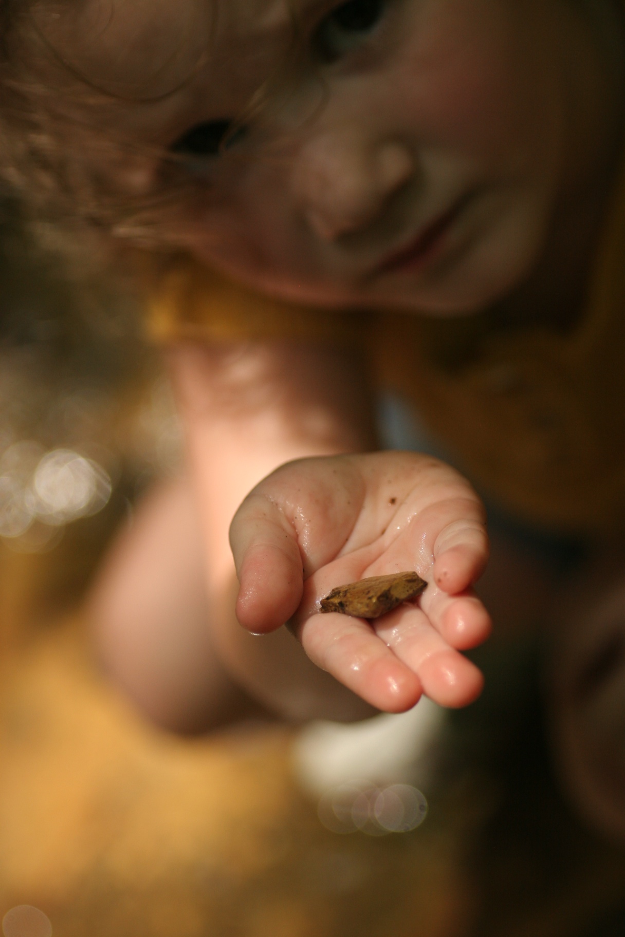 A toddler holding out a small stone in an open palm